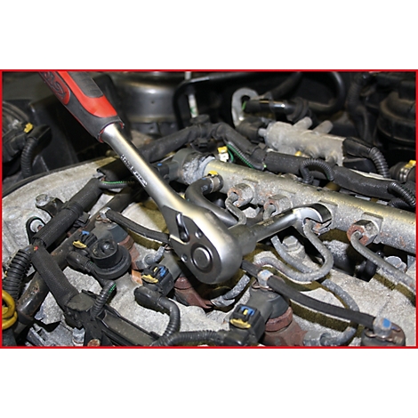 Eine Hand hält eine Ratsche, die an einem Motor arbeitet. Kabel und Rohre umgeben die Ratsche.